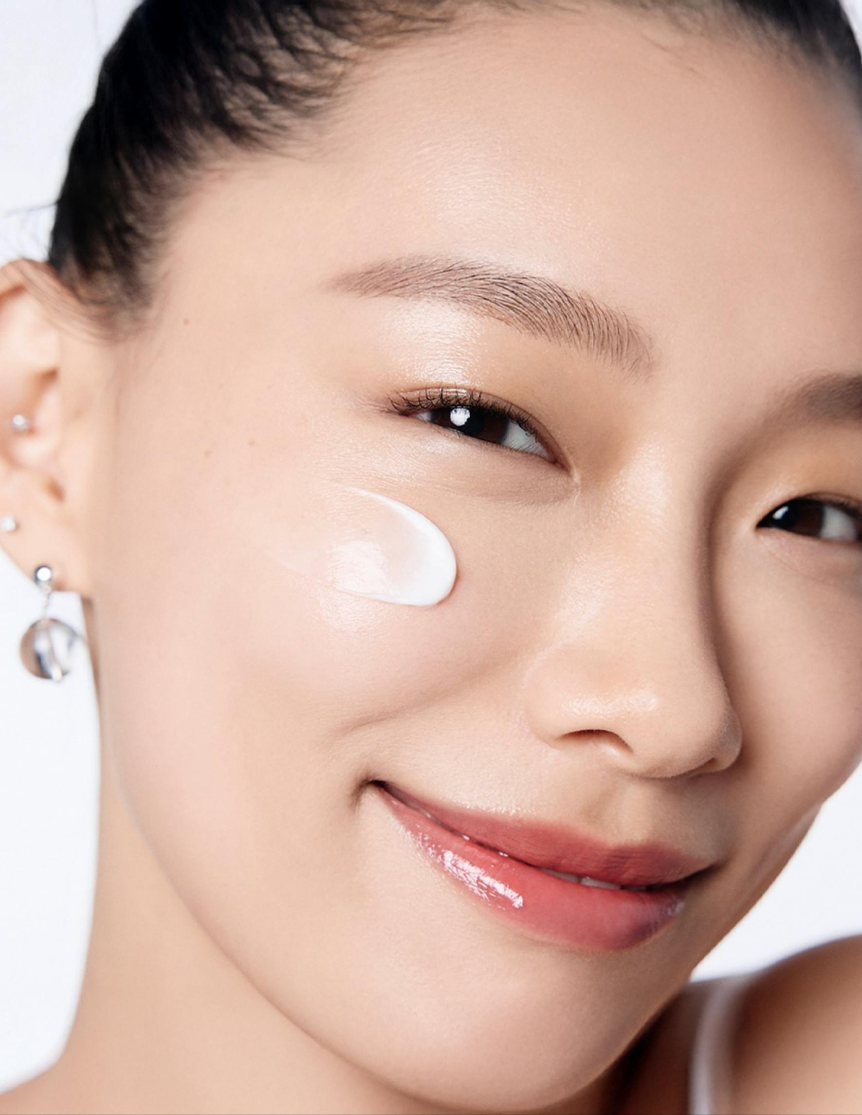 An Asian girl with some skincare product on her face.