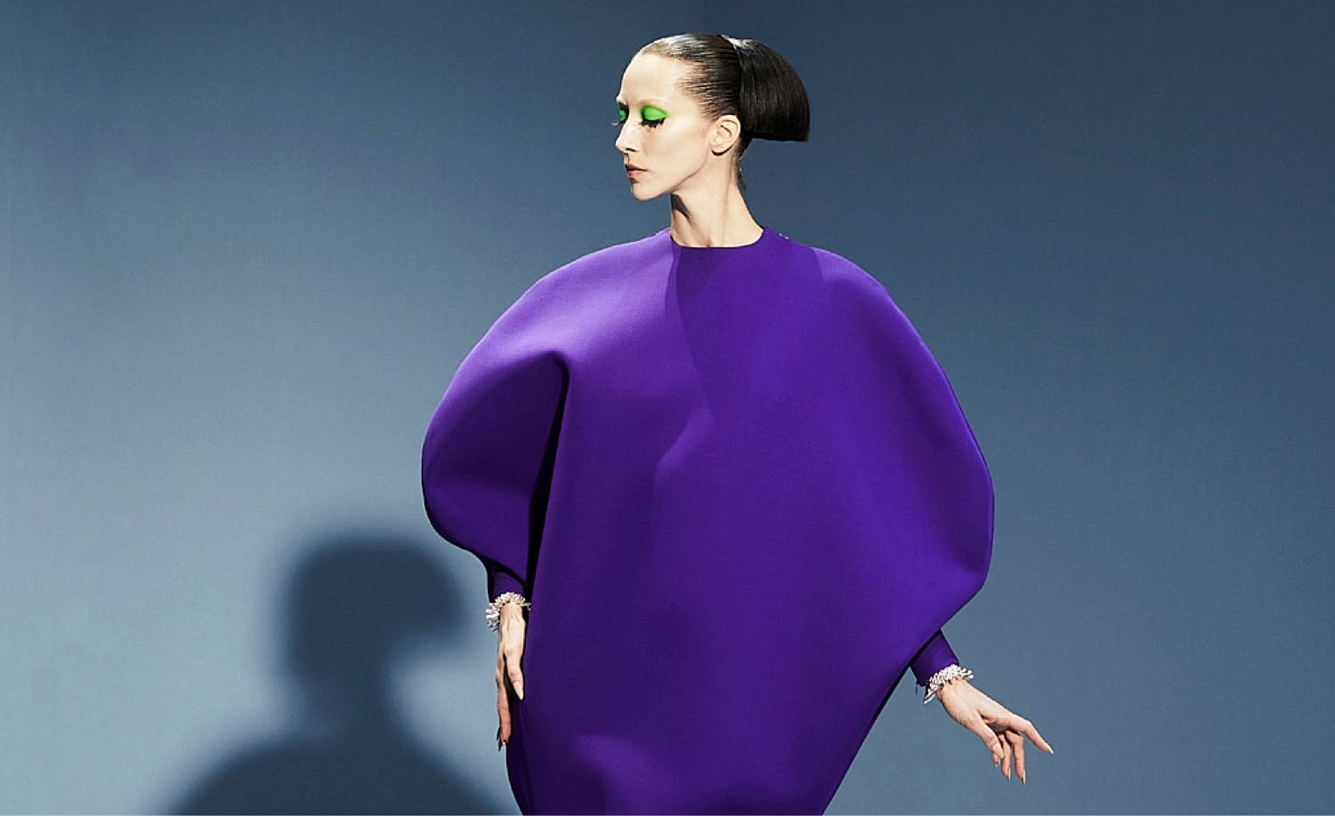 a woman in a purple dress posing in front of a blue background.