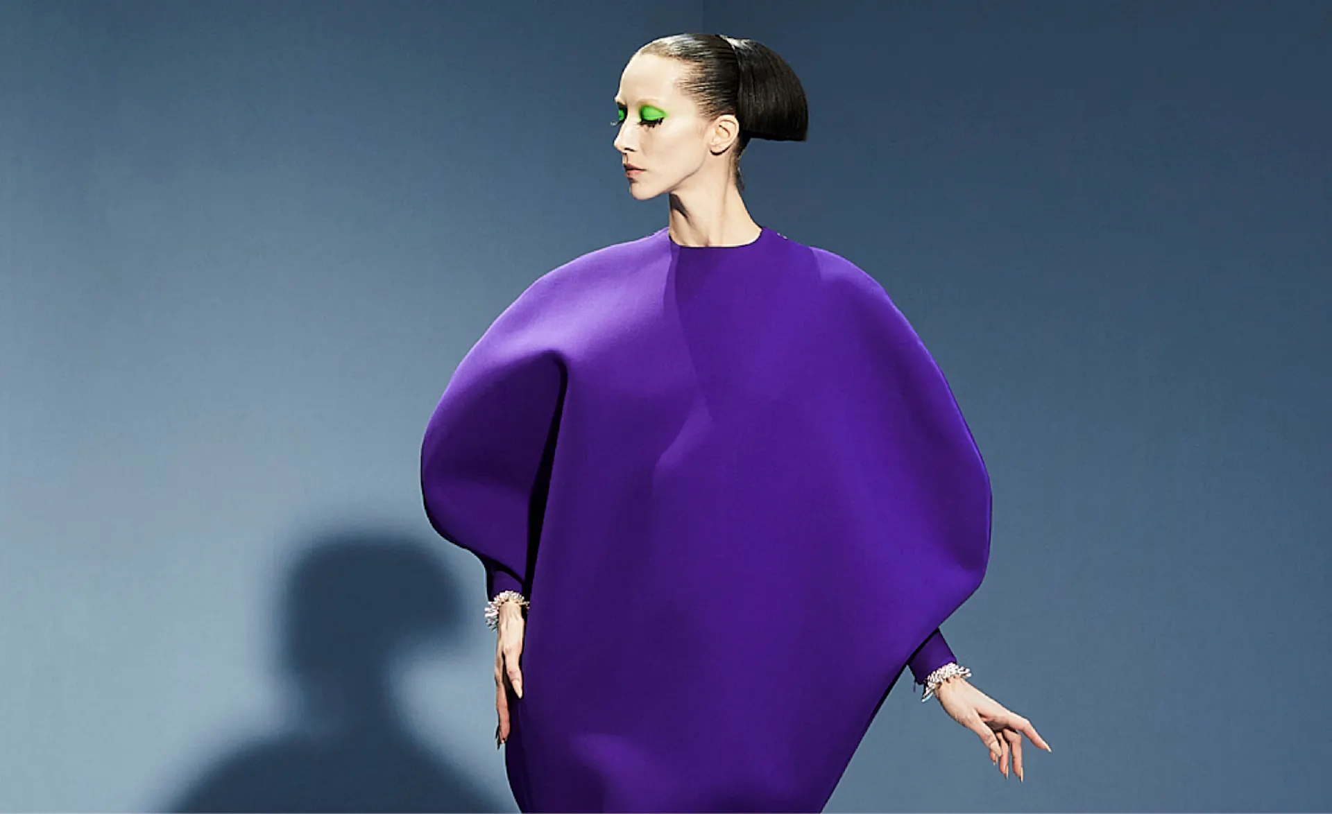 a woman in a purple dress posing in front of a blue background.