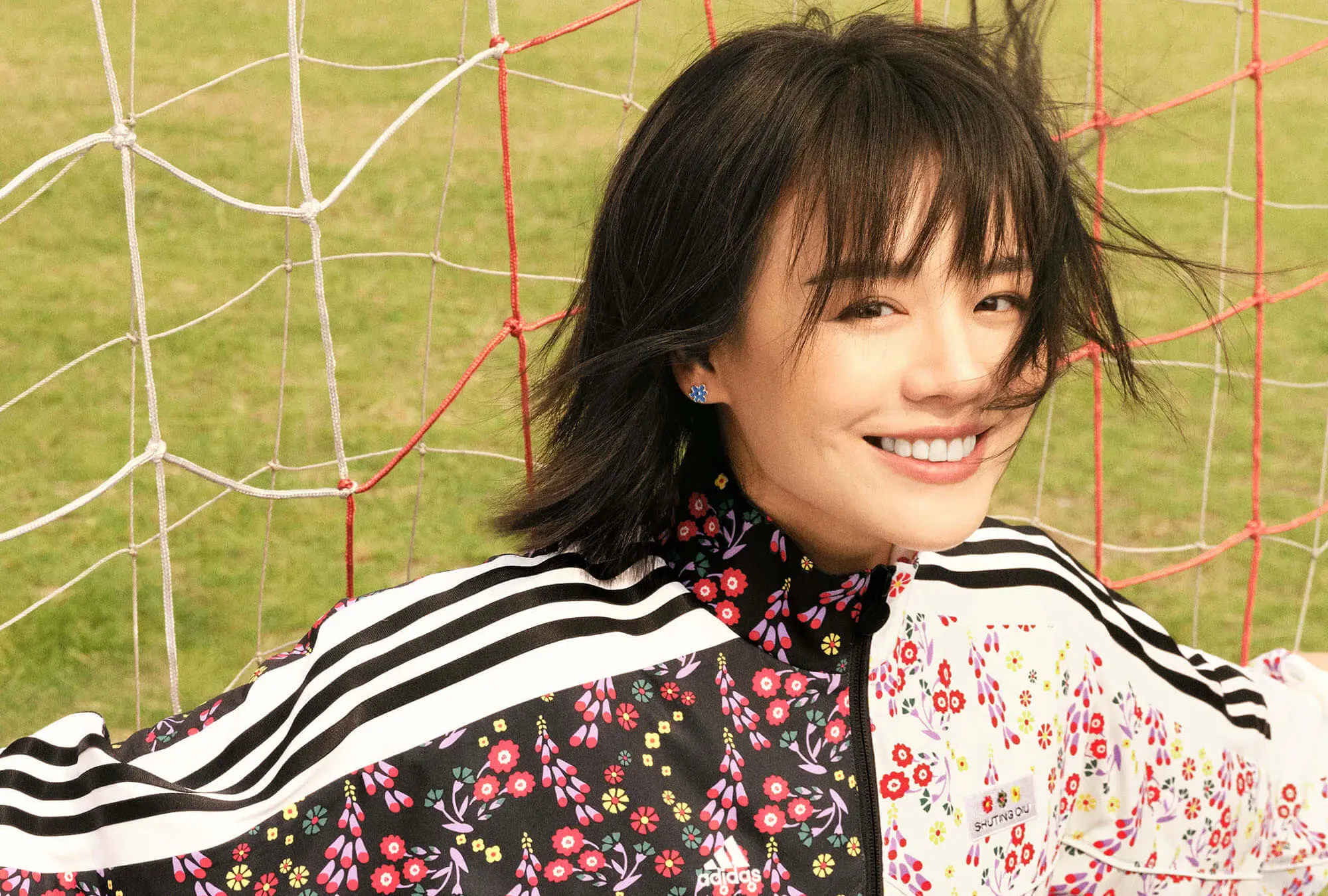 Photo of a woman in a floral adidas track jacket behind a football goal.