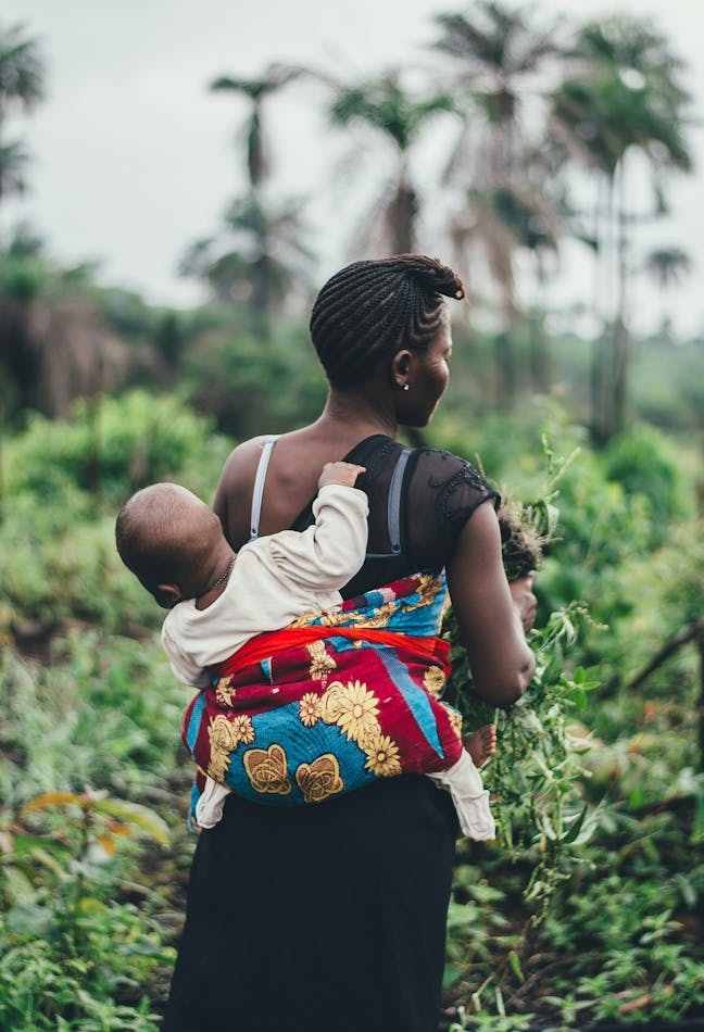 woman carrying child while harvesting food