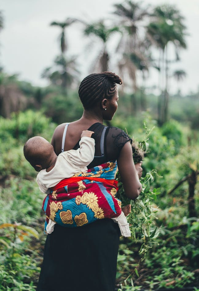 woman carrying child while harvesting food
