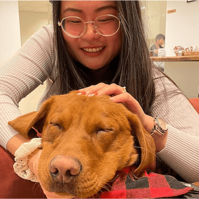 A smiling woman with glasses cuddling a golden labrador in the Lendable office. The dog is a very good boy.