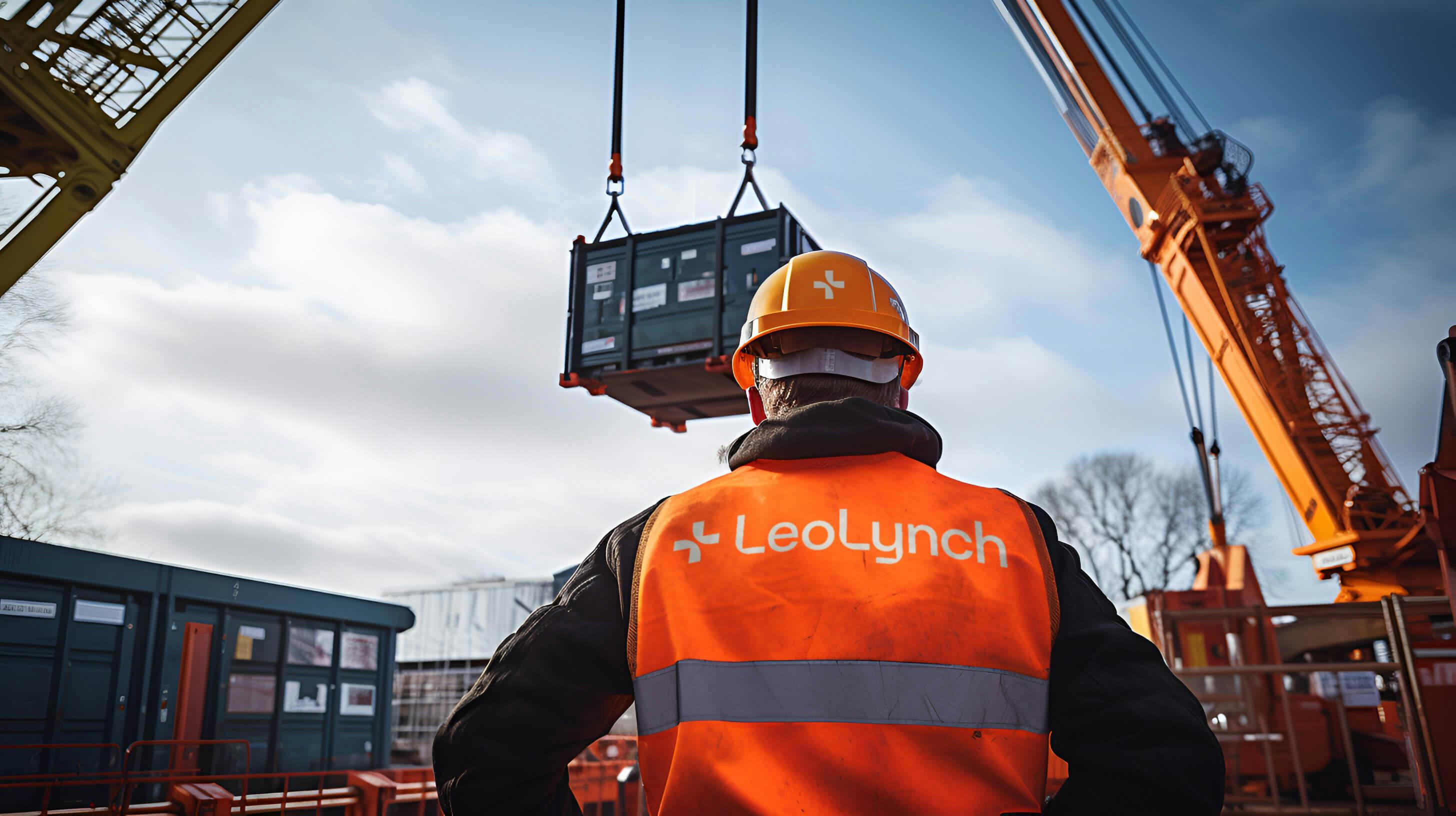 An engineer oversees a crane moving a shipping container. They are wearing Leo Lynch-branded 5 point PPE.