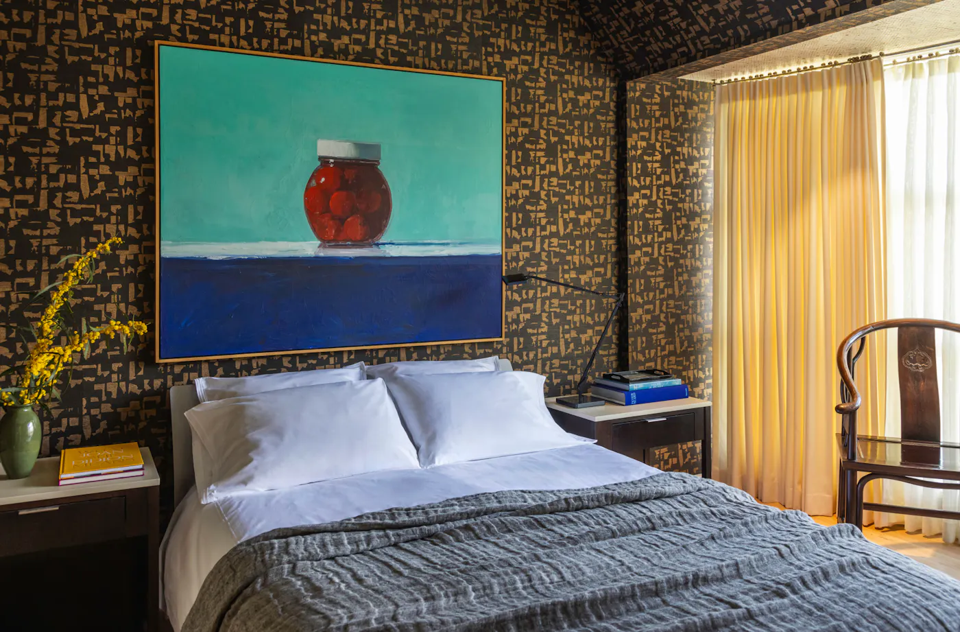 Eclectic bedroom design with patterned wallpaper, large-scale artwork, and layered bedding with warm natural light