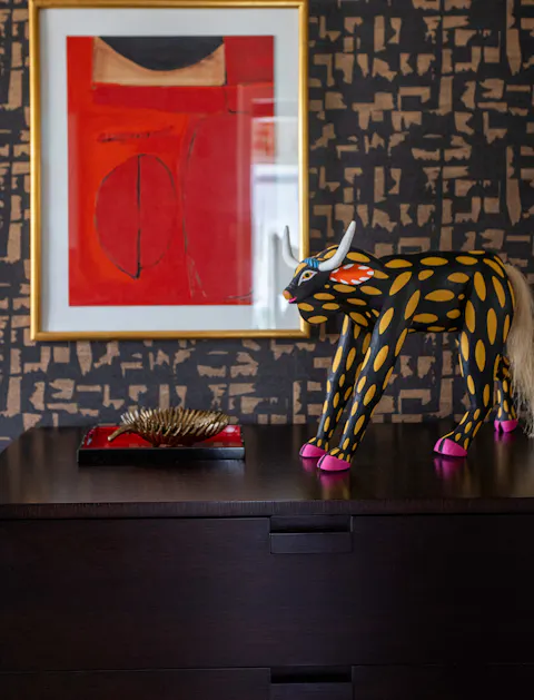 Eclectic interior styling with bold red abstract art, patterned wallpaper, and decorative sculptural accents on dark wood console