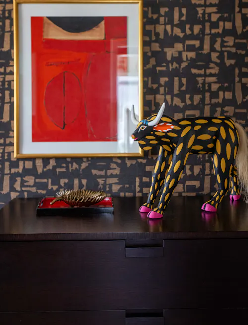 Eclectic interior styling with bold red abstract art, patterned wallpaper, and decorative sculptural accents on dark wood console