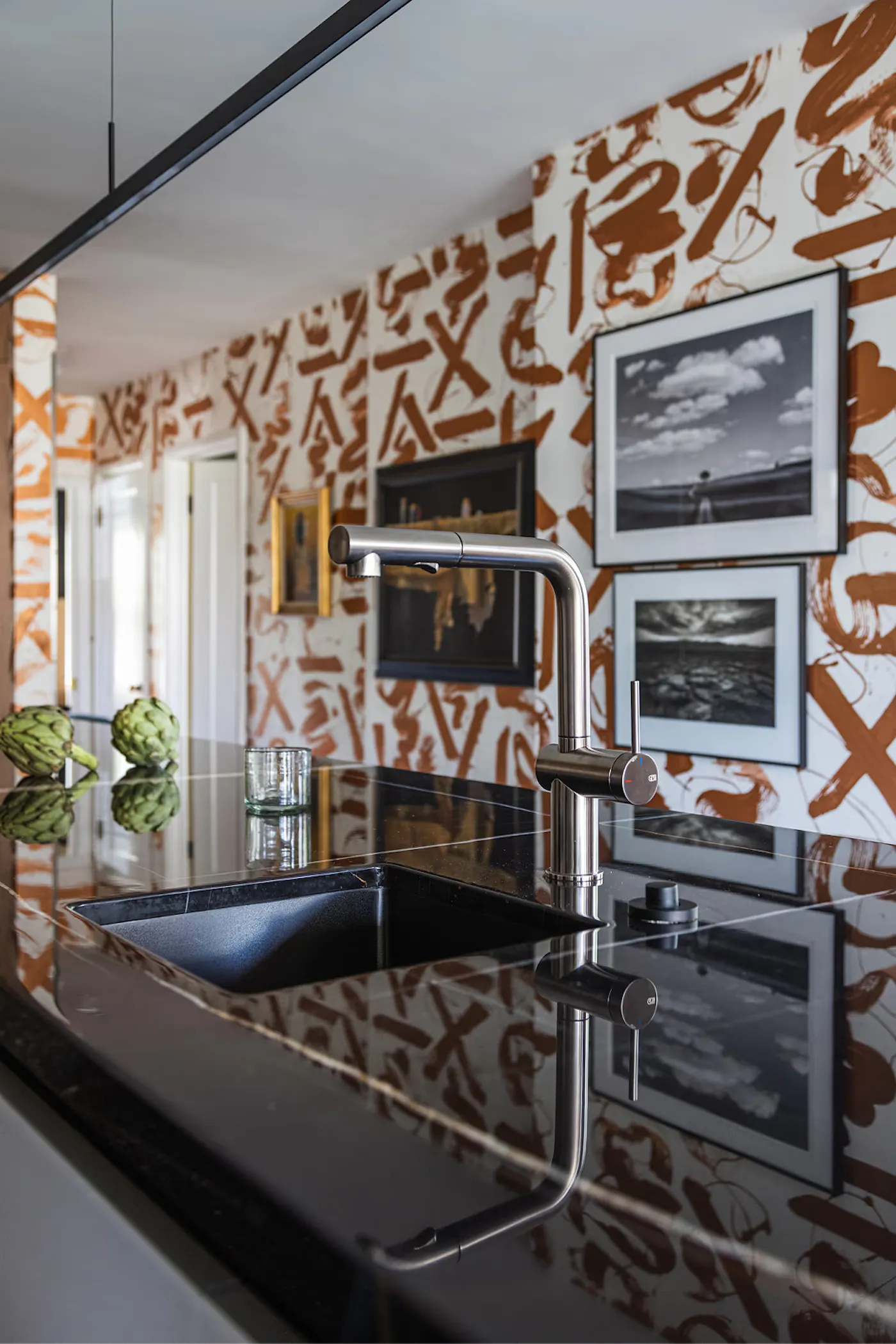 Modern kitchen detail with black stone countertop, integrated sink, stainless steel faucet, and abstract mural walls