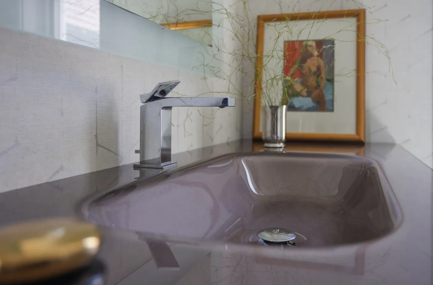 Modern bathroom detail with integrated sink, chrome faucet, and minimalist styling with framed artwork and greenery