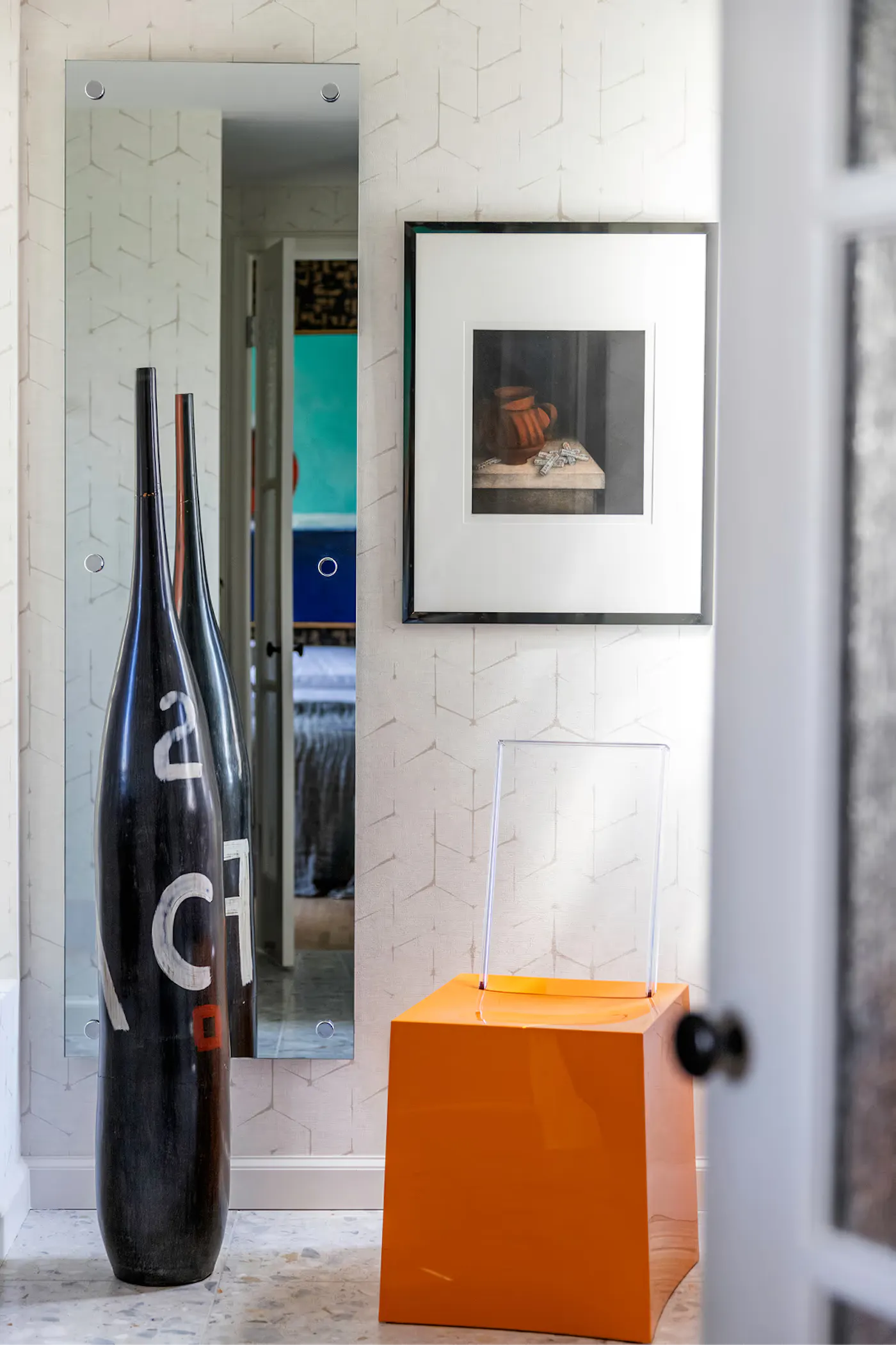 Interior design vignette with sculptural vases, wall mirror, framed artwork, and bold accent pedestal