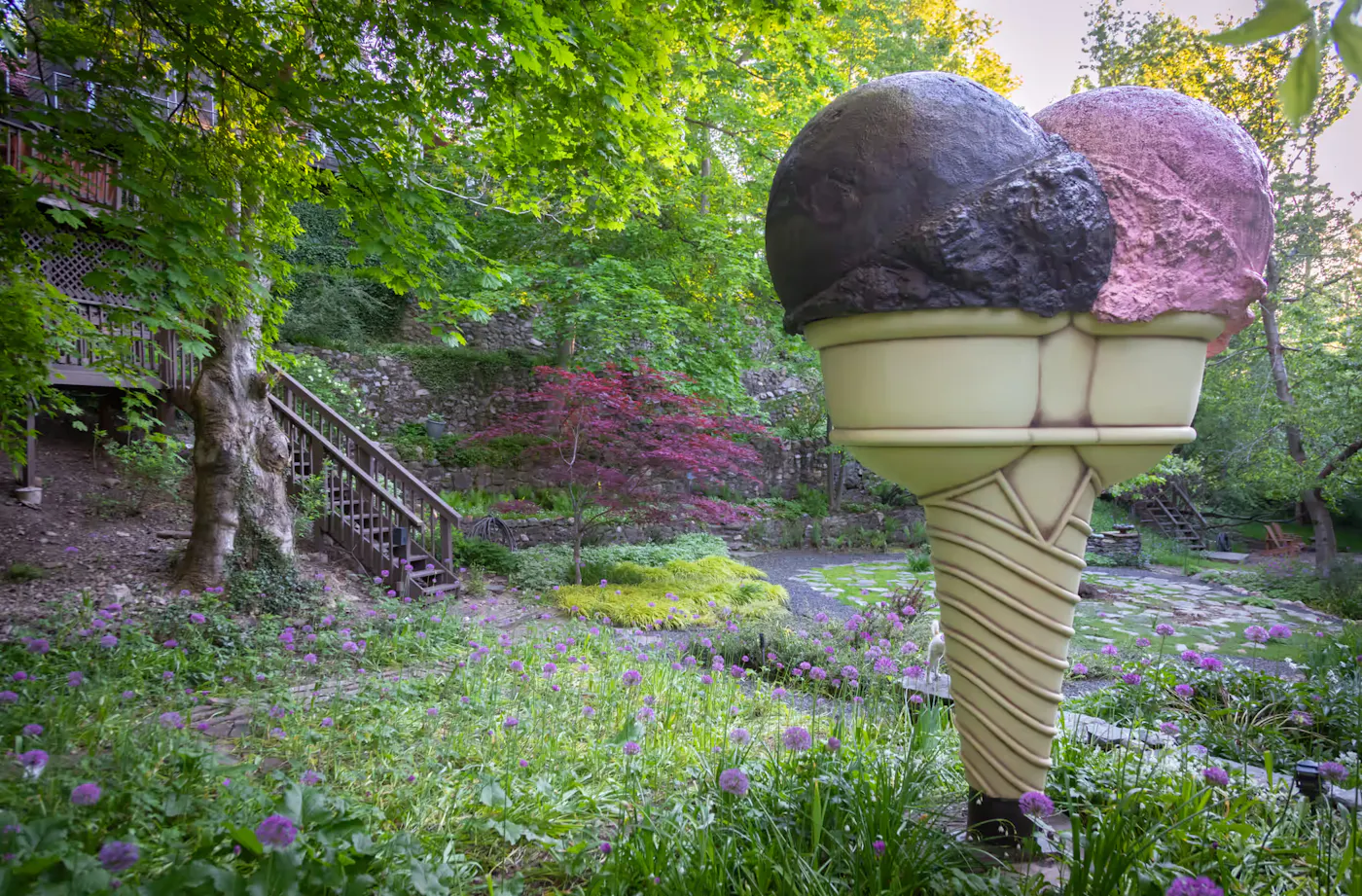 Landscape design with lush garden, stone pathways, and sculptural ice cream cone installation in natural setting