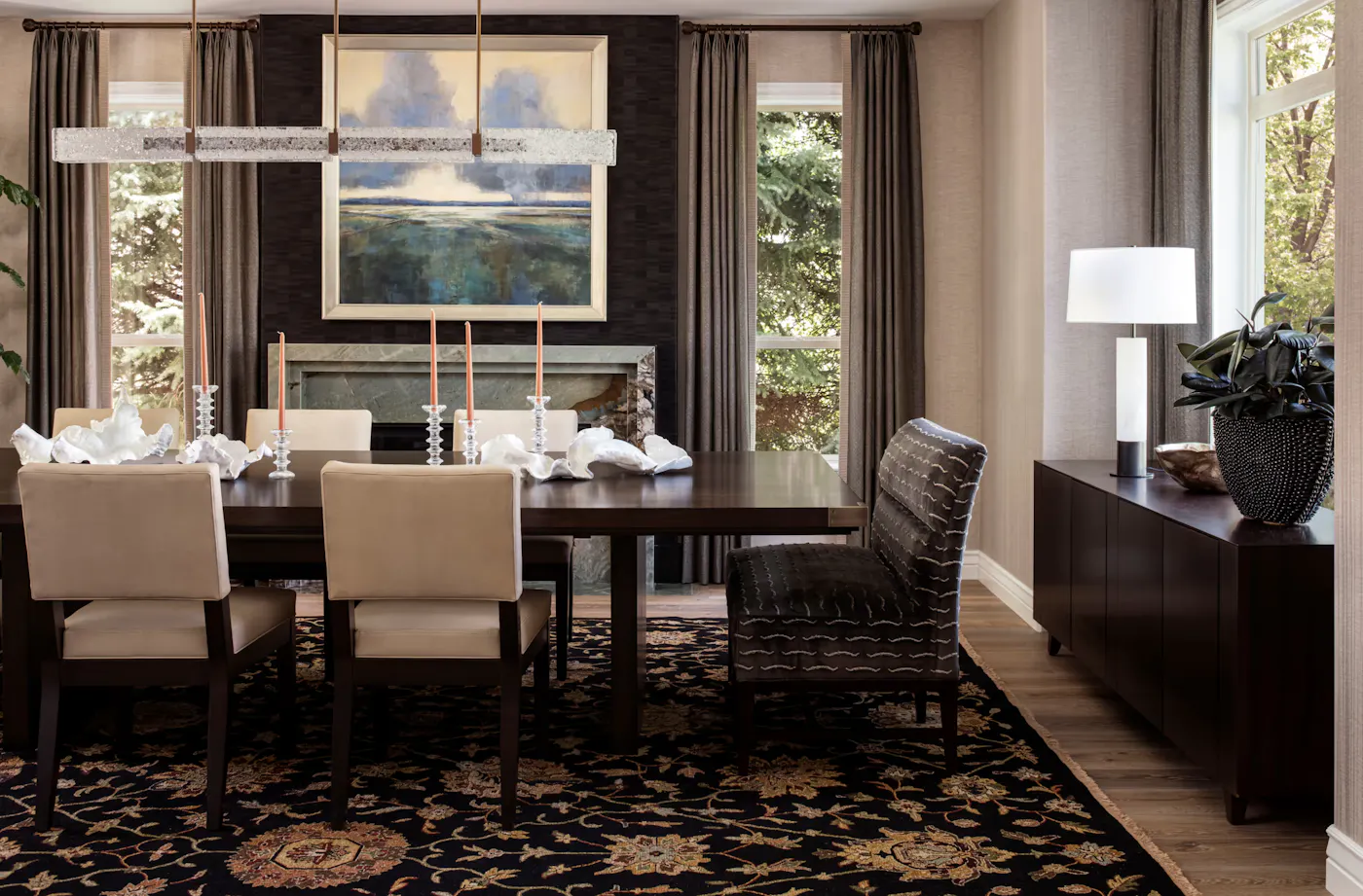 Dining room design with wood table, upholstered seating, statement lighting, and fireplace with artwork