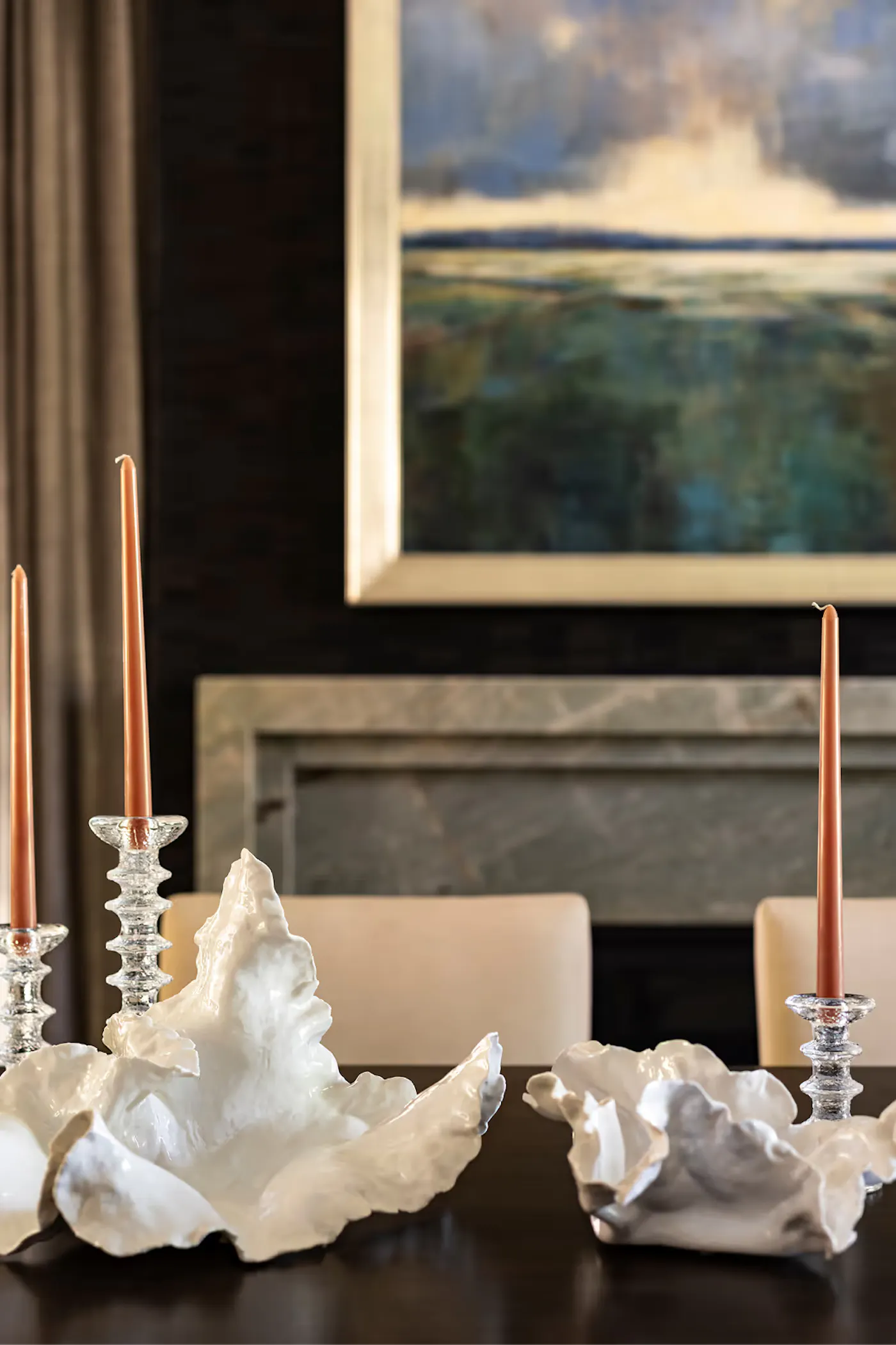 Dining table styling with sculptural decor, glass candlesticks, and warm tones in front of fireplace and artwork