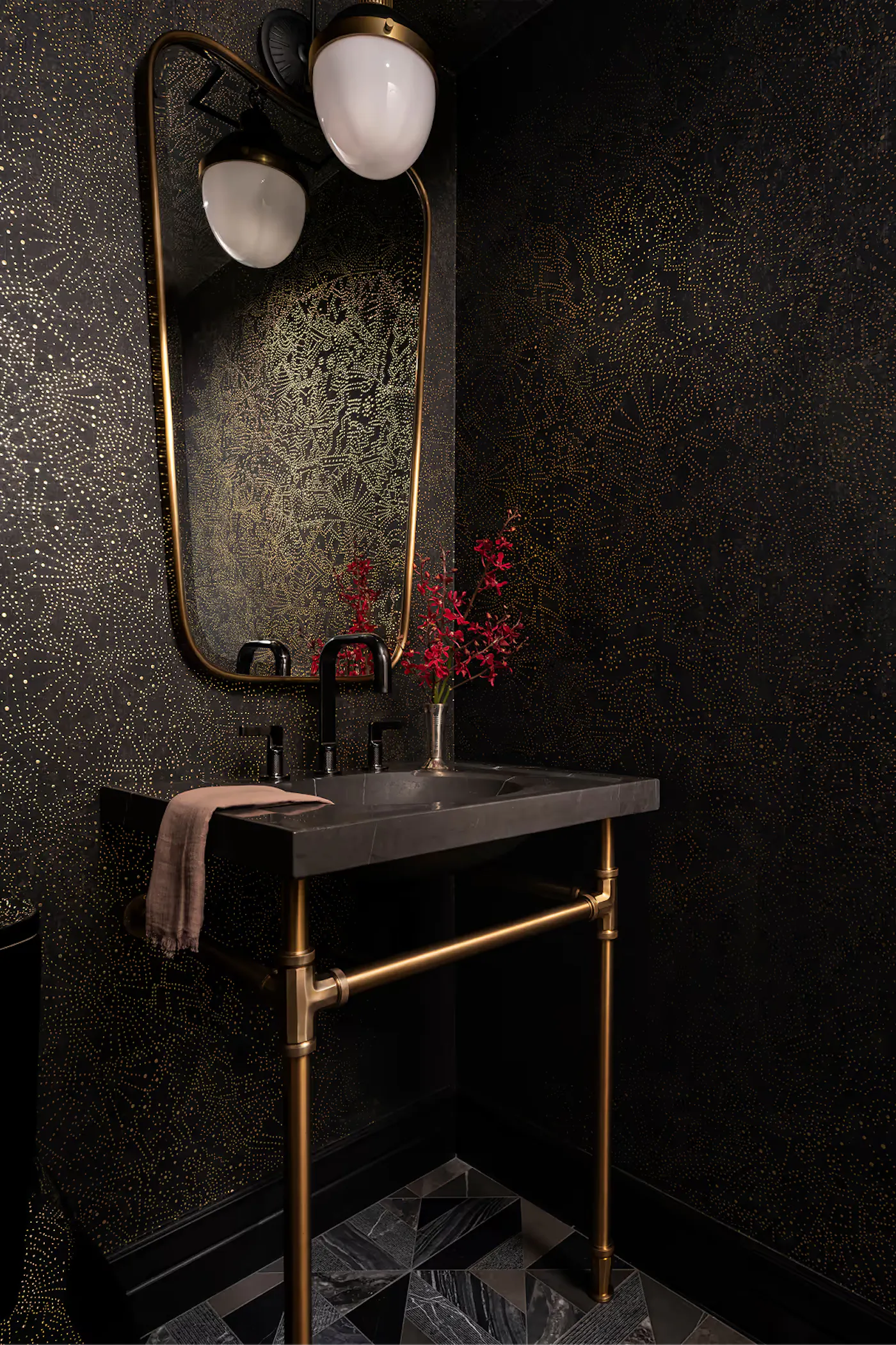 Moody powder bathroom with black textured walls, brass vanity, and sculptural lighting