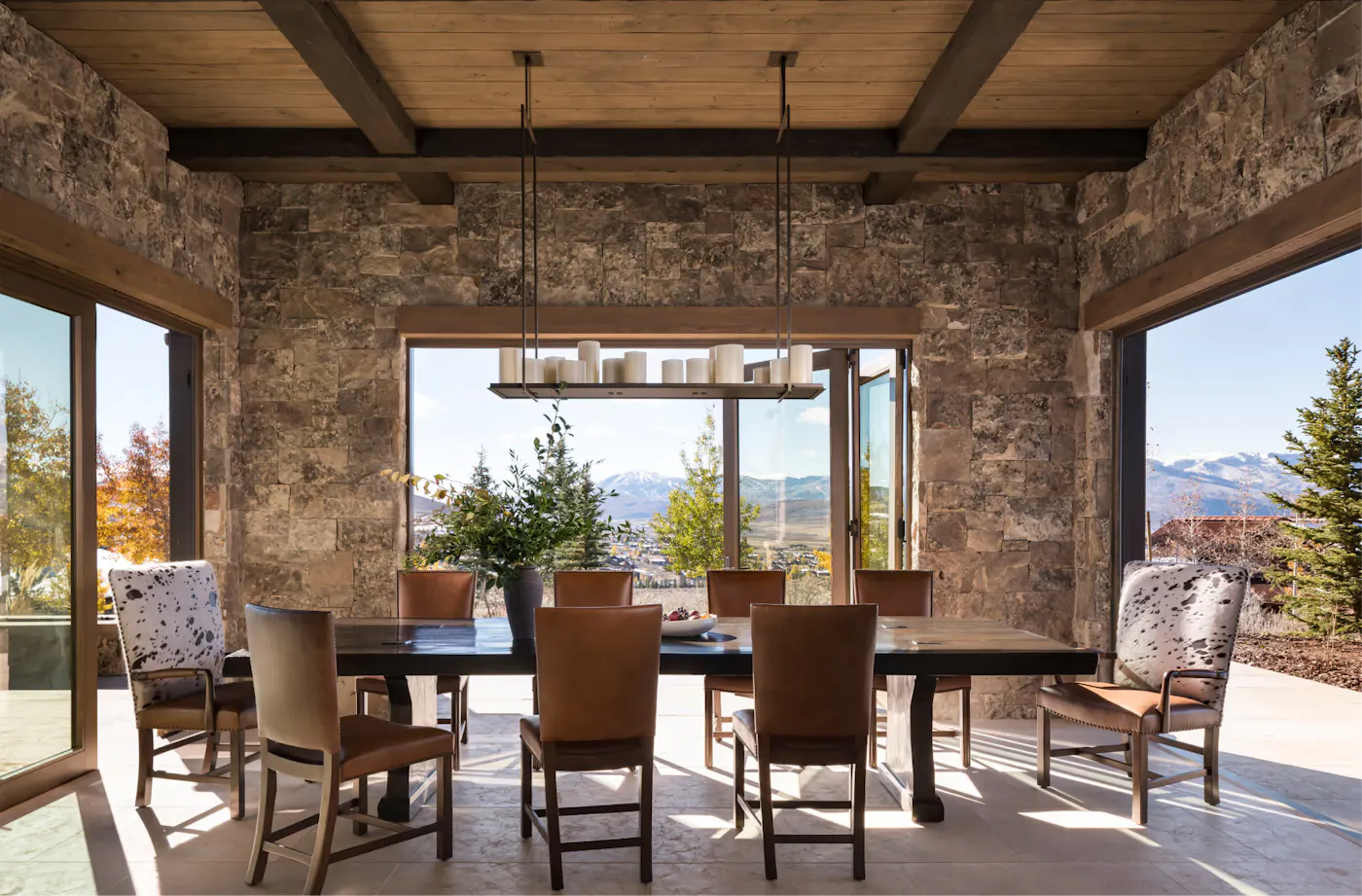 Dining room with exposed wood beams, stone walls, large windows, and panoramic mountain views