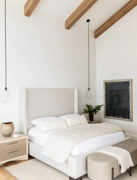 Modern neutral bedroom with upholstered bed, wood ceiling beams, and pendant lighting by Leslie Schofield Studio