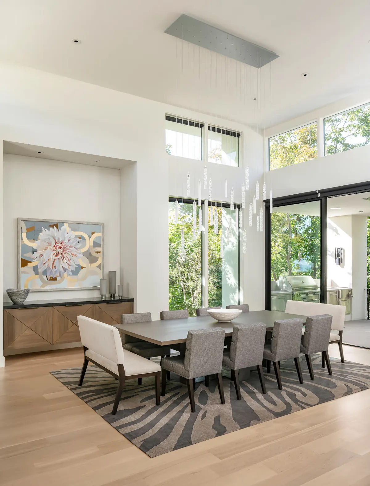Modern dining room with double-height windows, crystal chandelier, and contemporary seating by Leslie Schofield Studio