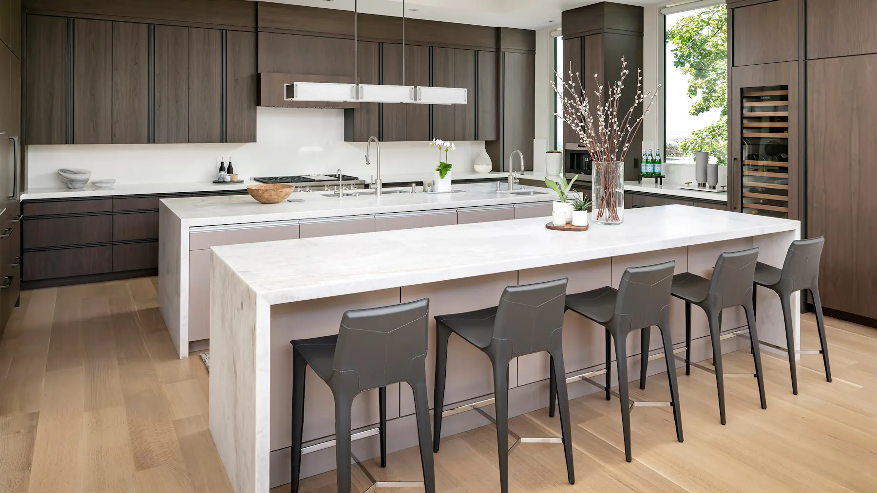 Modern luxury kitchen with dark wood cabinetry, double marble islands, and bar seating by Leslie Schofield Studio