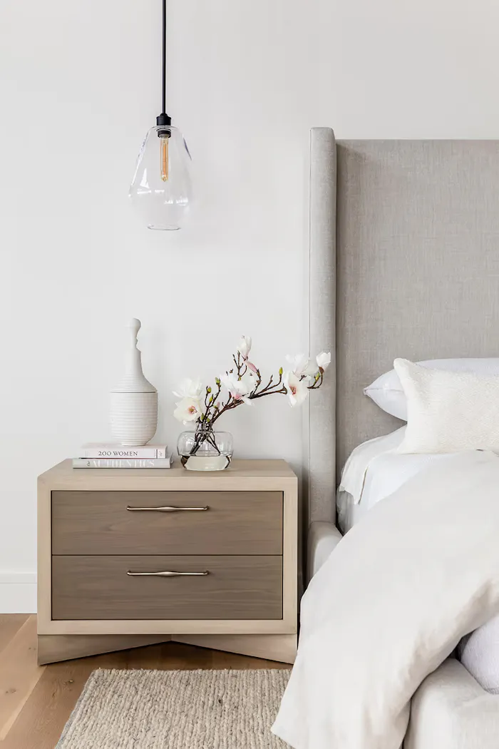 Elegant modern bedroom detail with textured linen headboard, light wood furnishings, and minimalist floral styling
