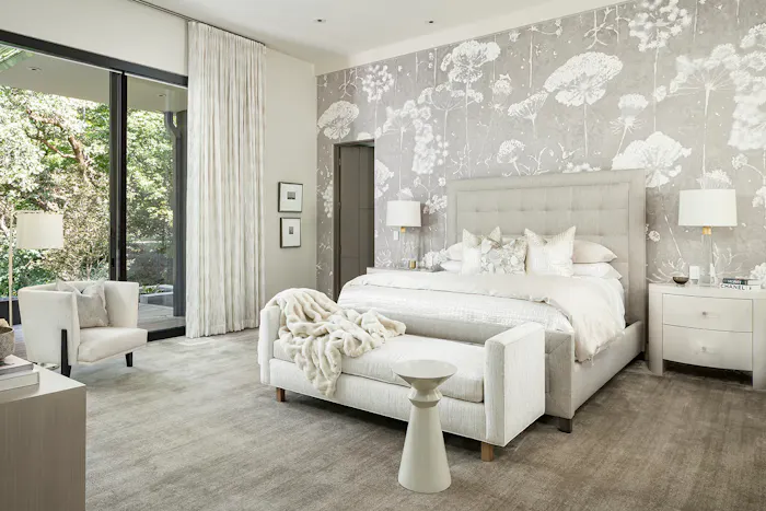 Modern luxury bedroom with serene neutral palette, upholstered bench seating, and large sliding glass doors overlooking landscaped greenery