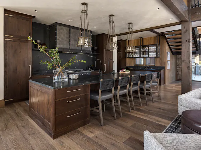 Rustic luxury kitchen with dark wood cabinetry, oversized black stone island, and custom pendant lighting by Leslie Schofield Studio