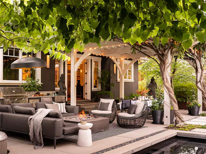 Luxury outdoor living space with covered patio, modern lounge seating, fire pit, and lush landscaped garden by Leslie Schofield Interiors