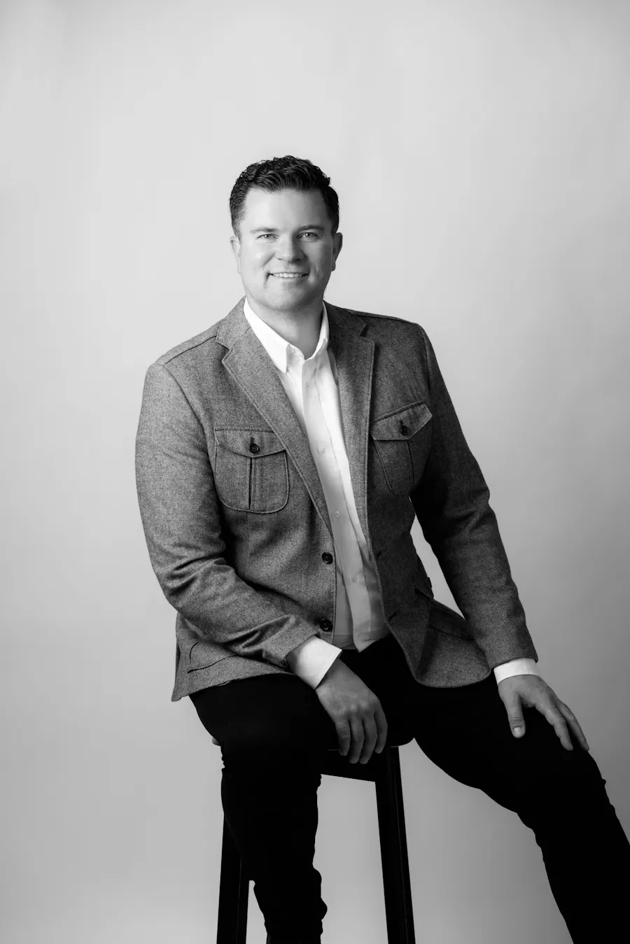 Black and white portrait of interior designer Matt Dickamore seated on stool