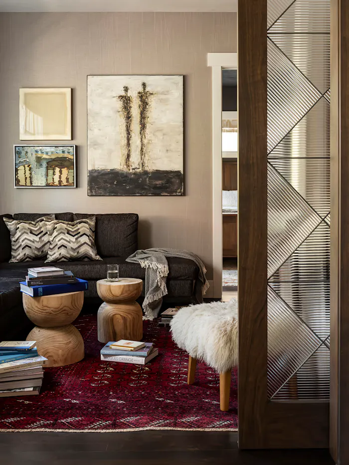 Contemporary living room interior featuring layered abstract artwork, sculptural wood accent tables, and a rich vintage-inspired red area rug