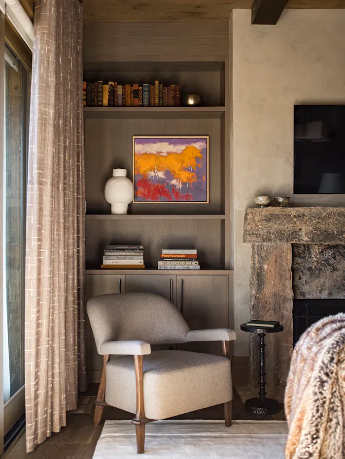 Cozy luxury living room reading nook featuring custom built-in shelving, textured neutral furnishings, and a rustic stone fireplace