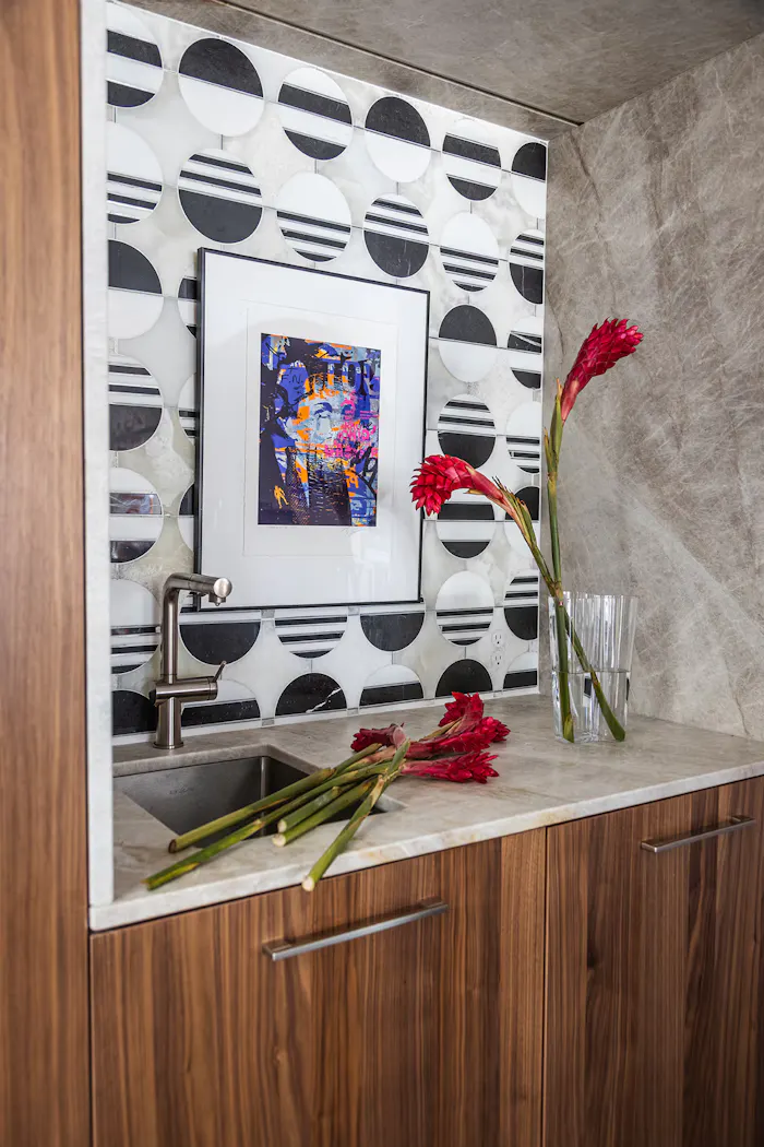 Contemporary wet bar design featuring geometric black and white tile backsplash, walnut cabinetry, and vibrant floral styling accents