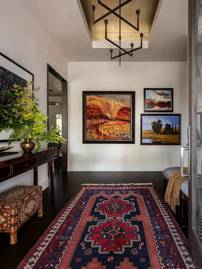 Sophisticated foyer interior with gallery-style wall art, traditional patterned rug, and dramatic contemporary lighting in an upscale residential space