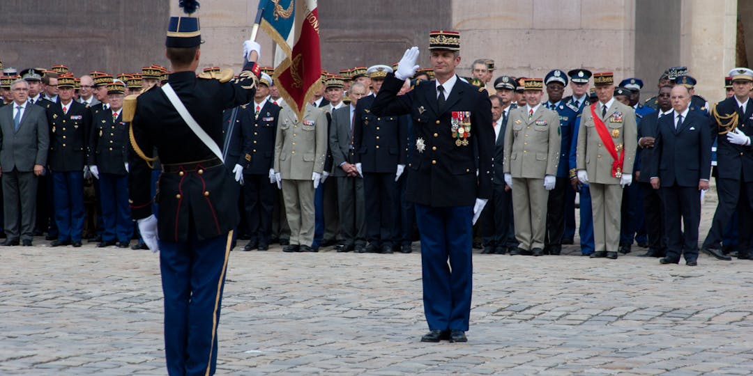 Jérome Favier, alors élève-officier (de dos), portant le drapeau de la Gendarmerie le 30 aout 2016 dans la cour d'honneur des Invalides, devant le général d'armée Denis Favier, son père, lors de l'Adieu aux armes de ce denier (M.GUYOT/ESSOR)