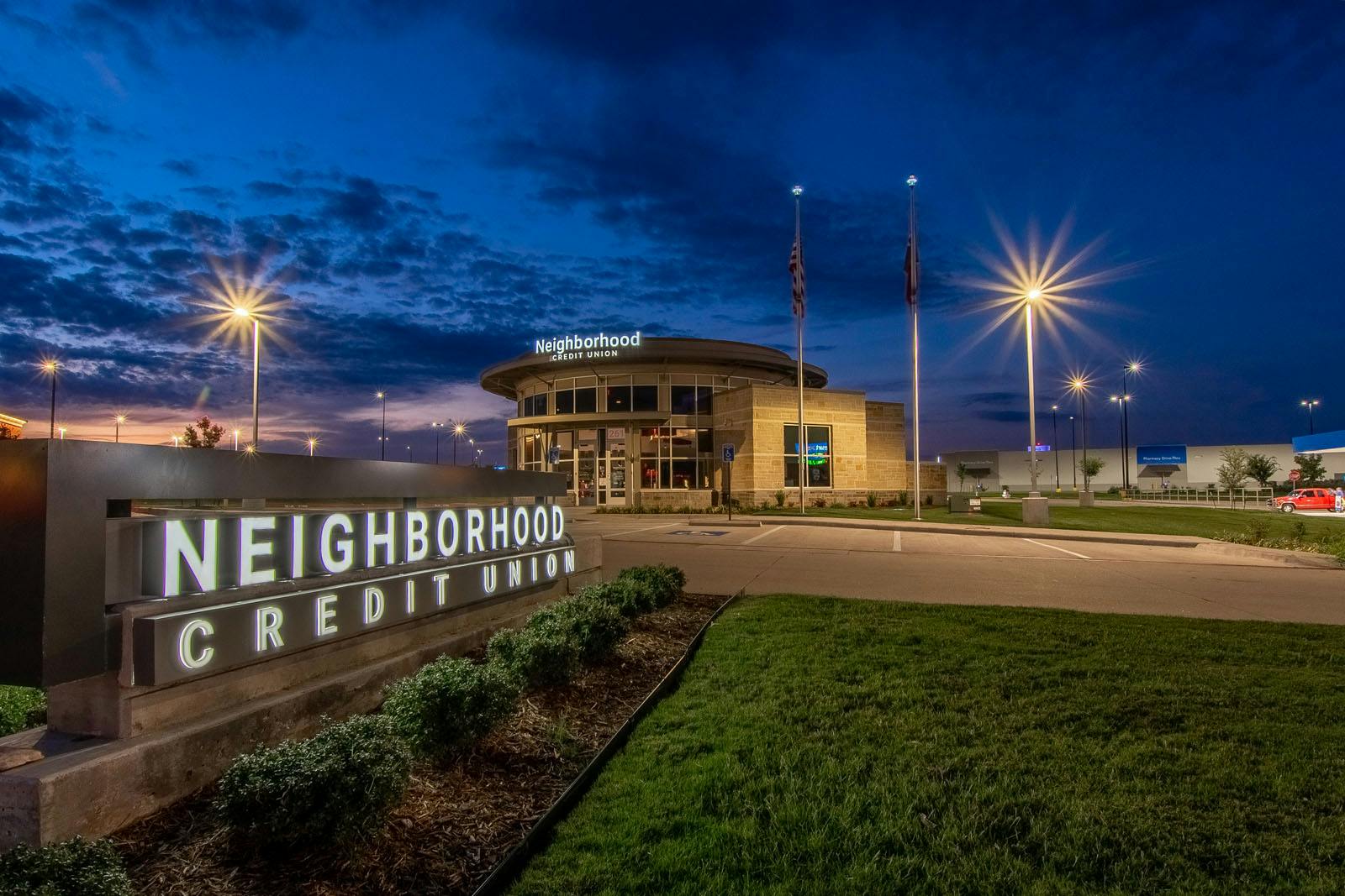 The Neighborhood Credit Union road sign with the credit union building behind it in the late evening