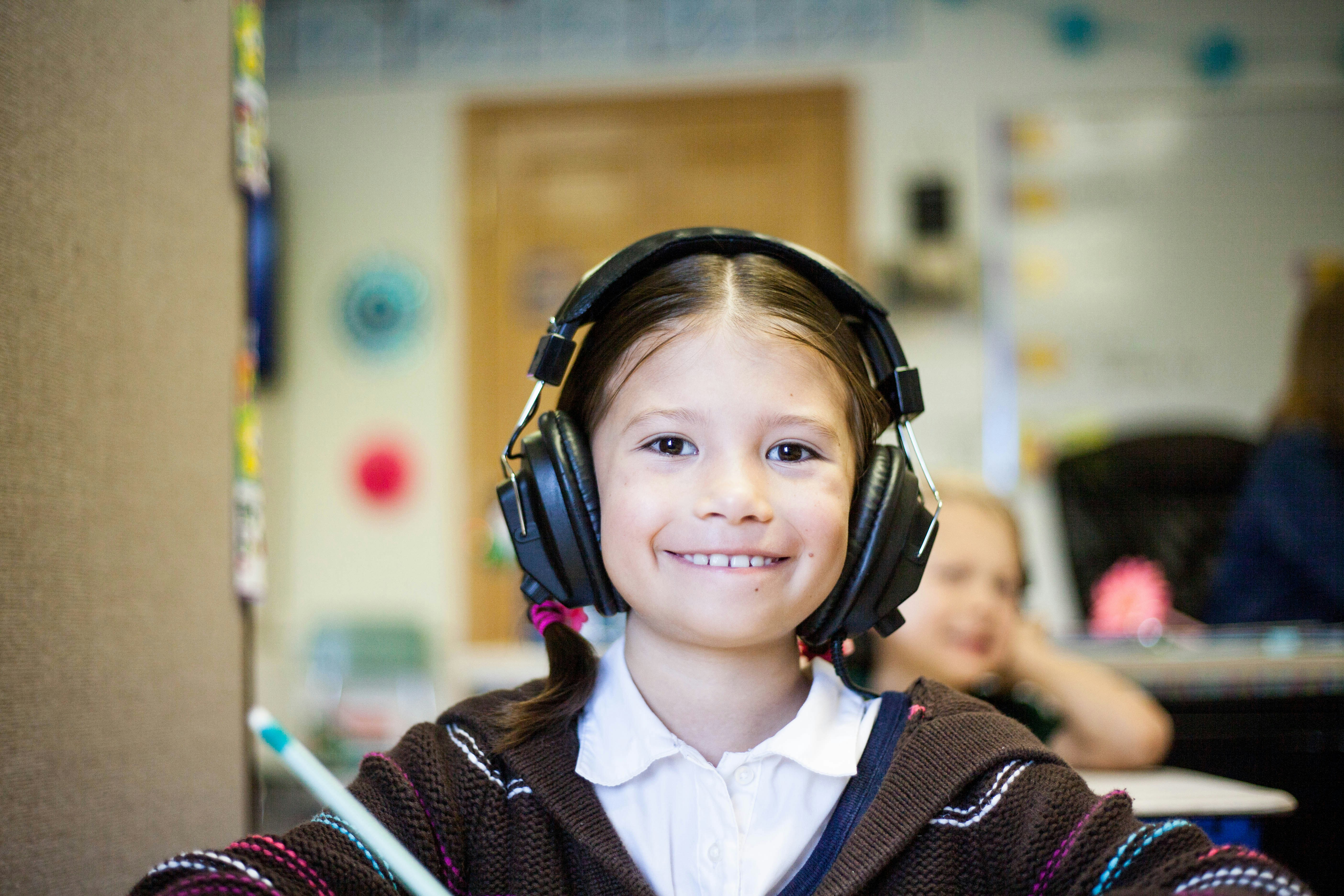 Photo of a smiling child in a classroom wearing headphones
