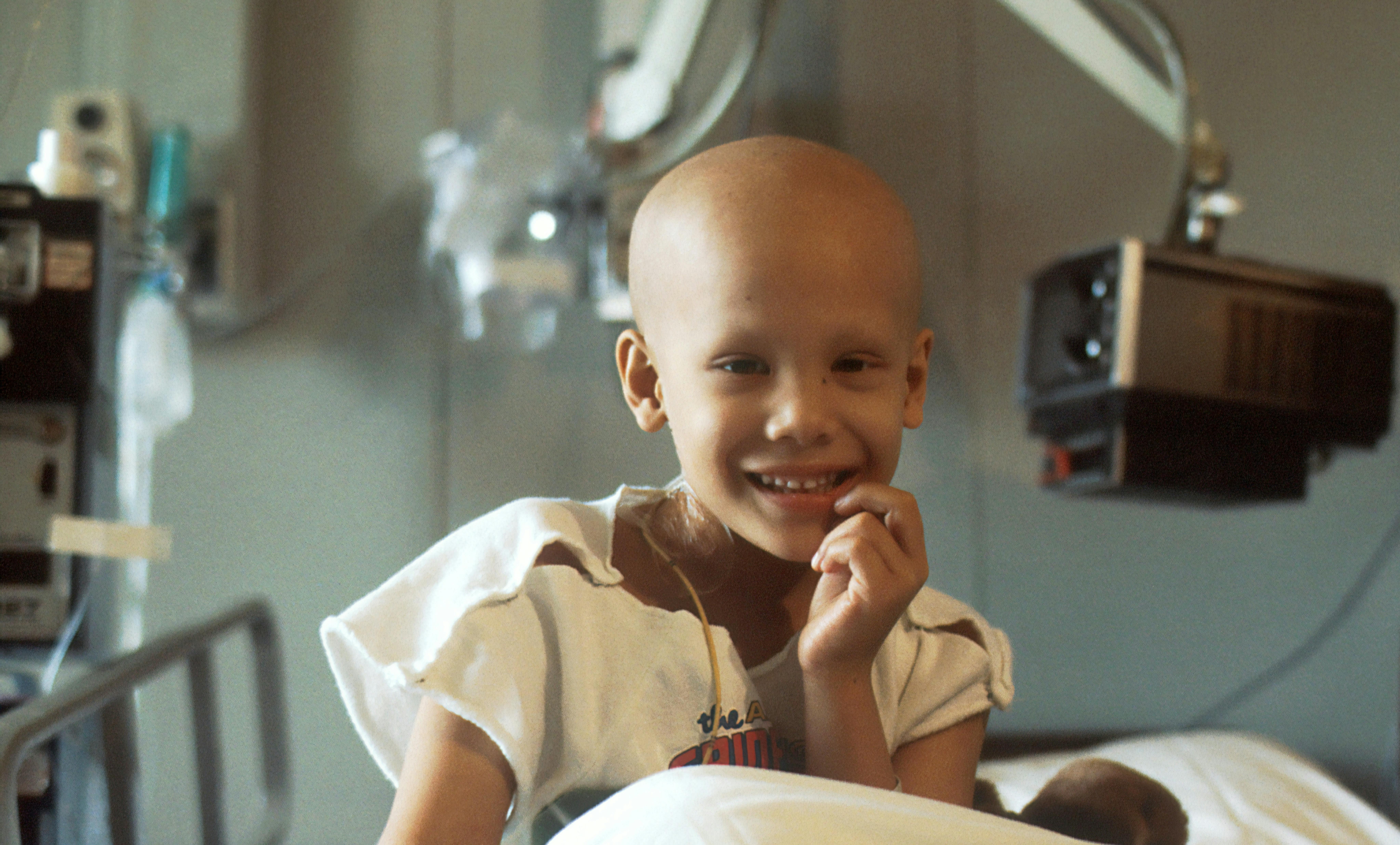 Photo of smiling childhood cancer treatment patient sitting up in her hospital bed
