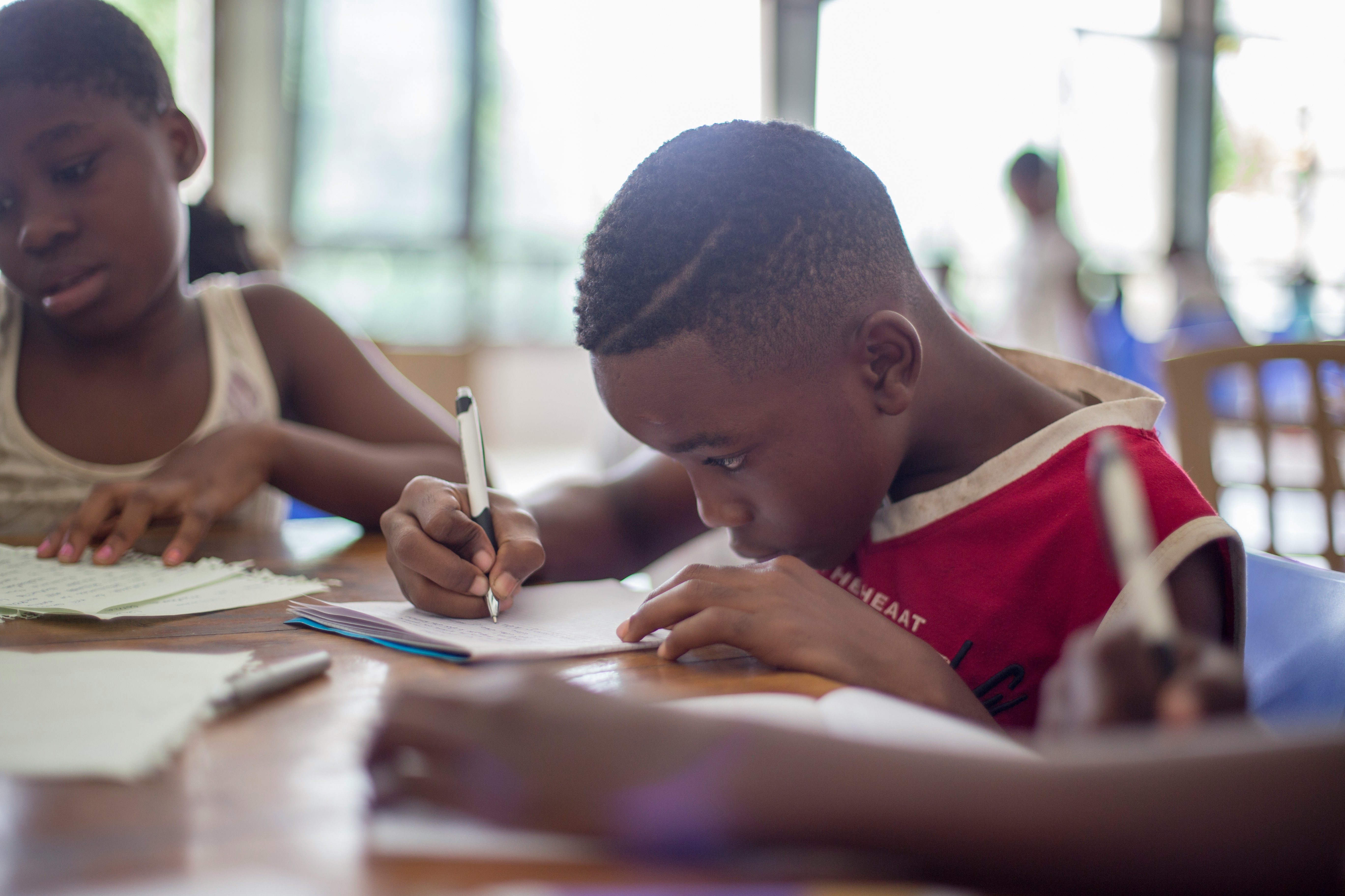Photo of a boy writing and girl writing at at table at school