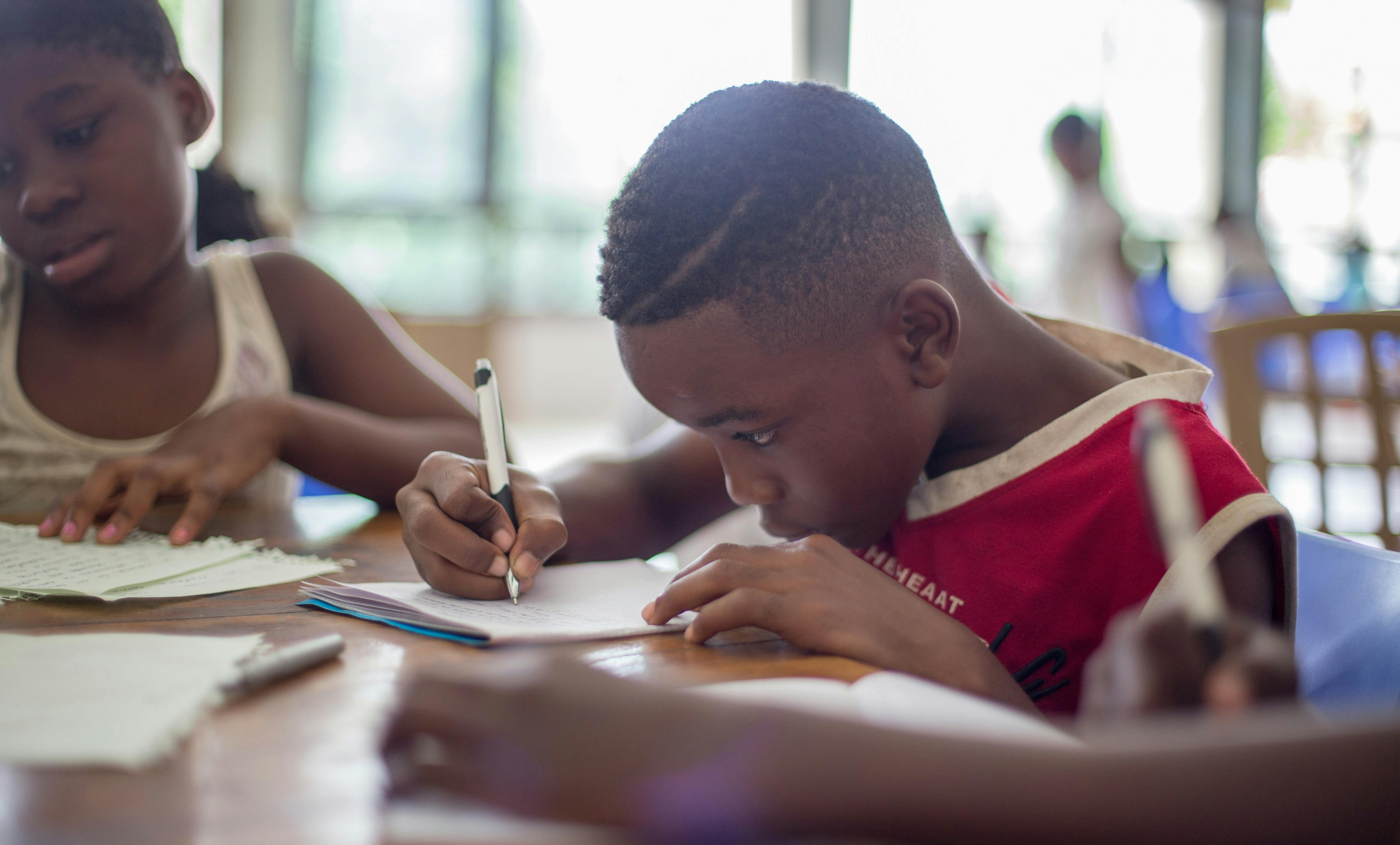 Photo of a boy writing and girl writing at at table at school