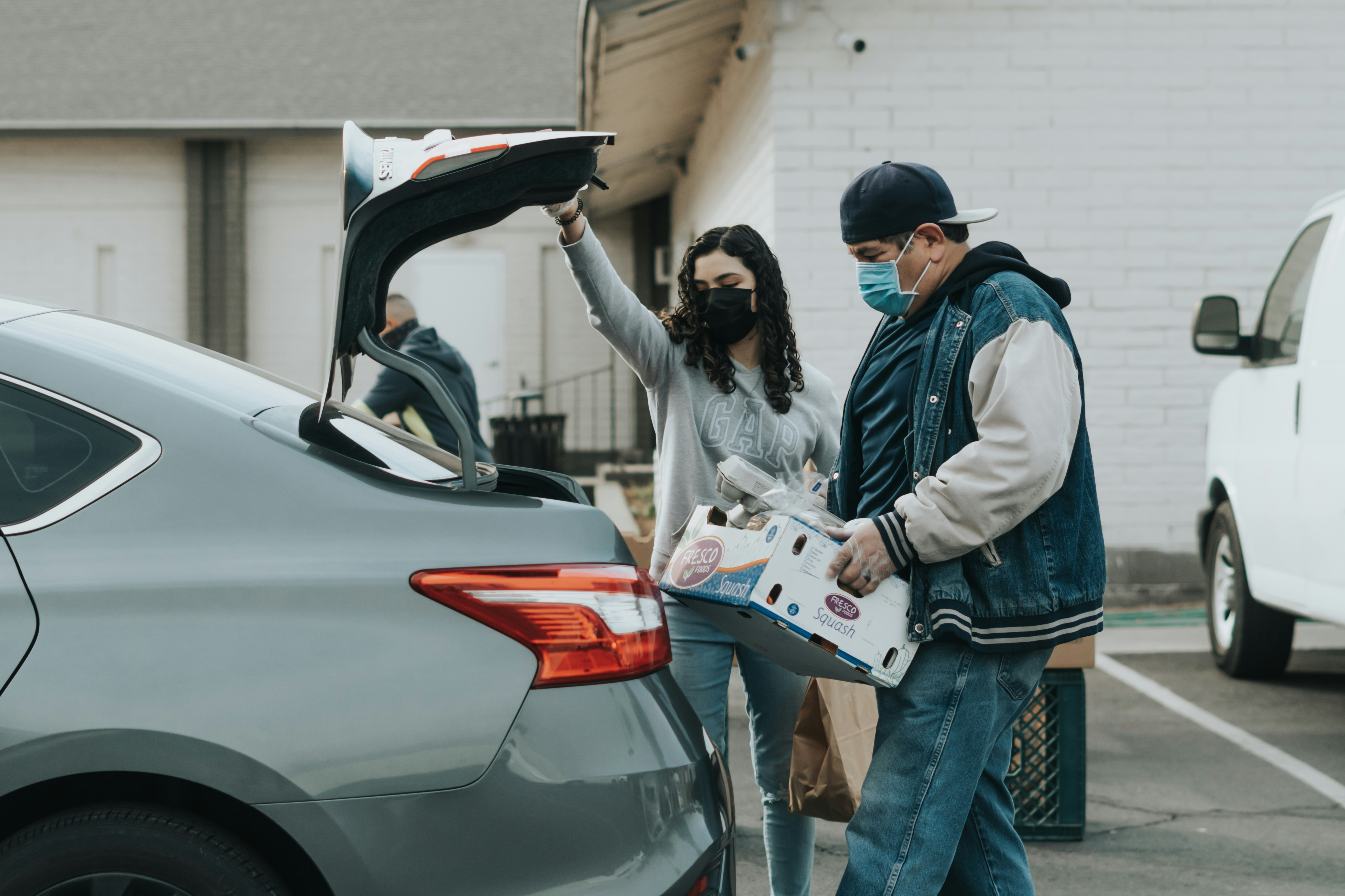 Two people unloading food items from the trunk of a car