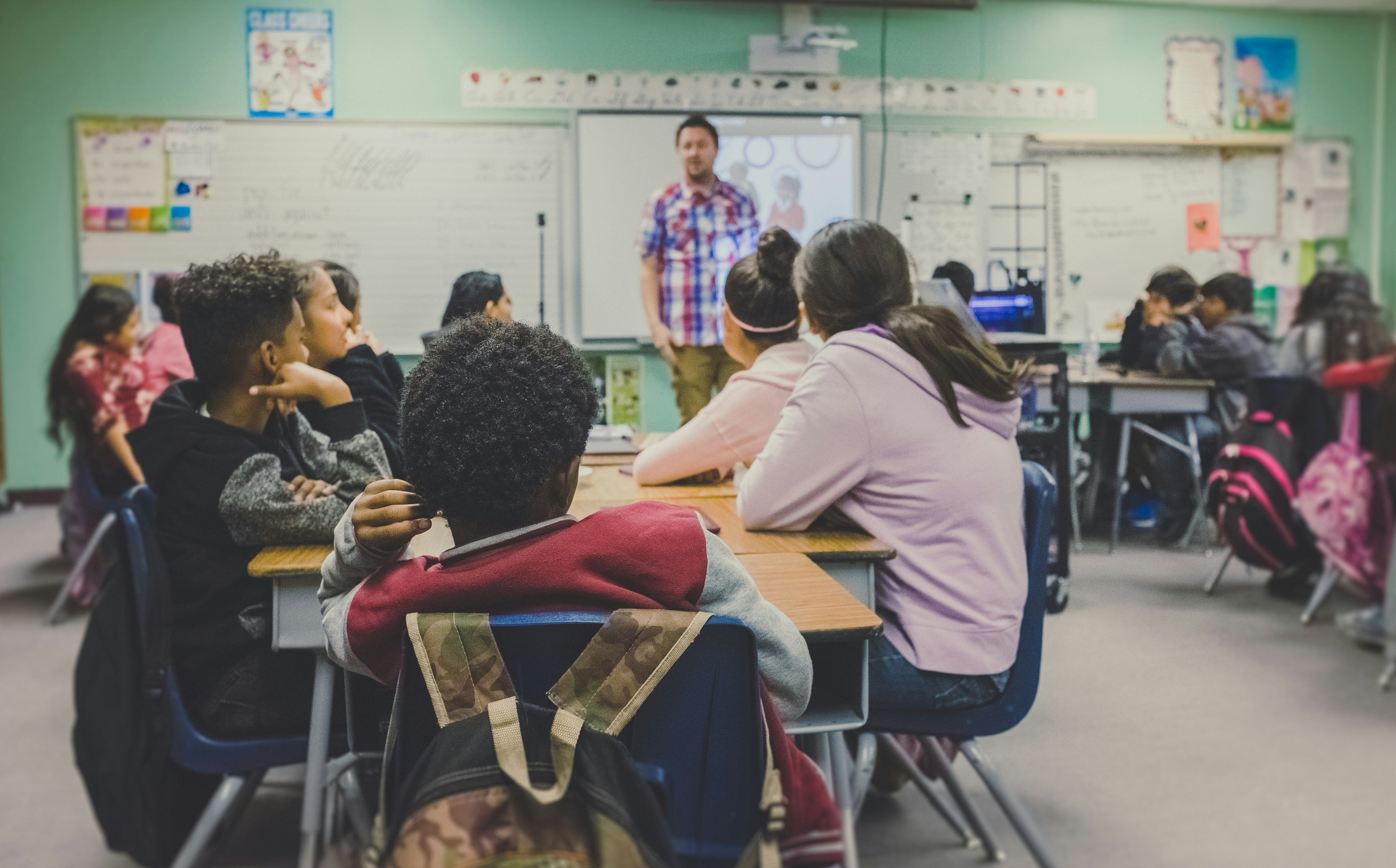 Photo of a classroom with students at tables and a teacher at the front of the room