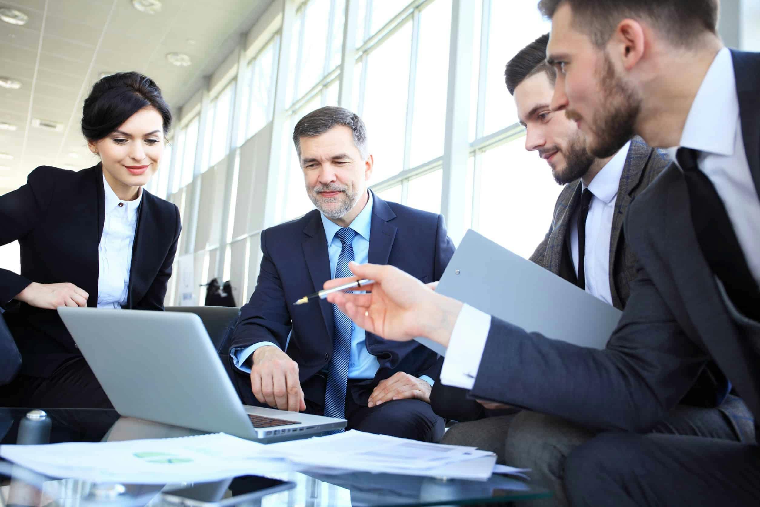 4 business people in a discussion over information on a laptop screen.