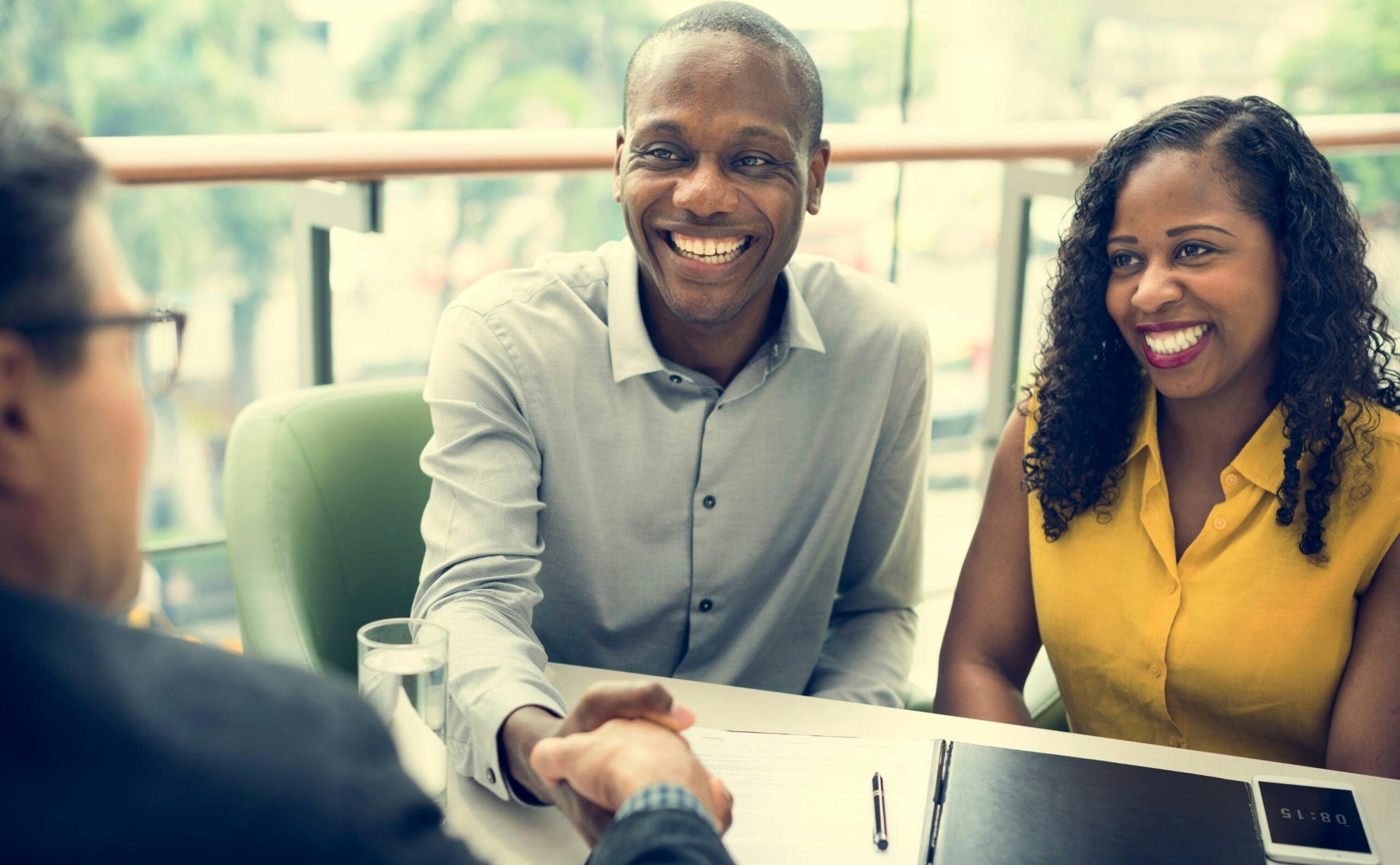 A couple smiling a shaking hands with a bank representative