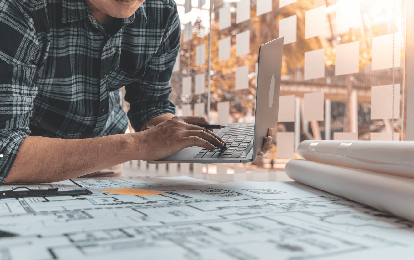 male holding a laptop and leaning over floor plans