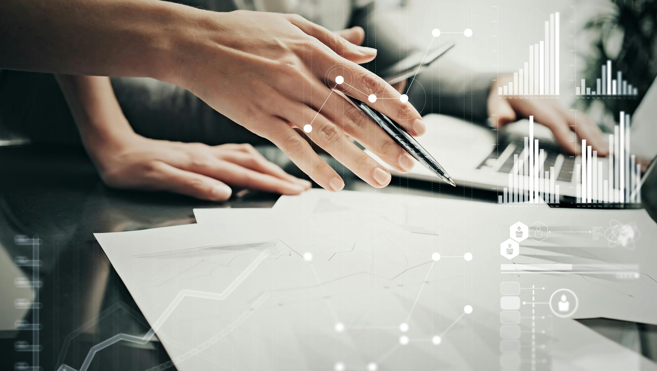 A hand holding pen hovering over papar. Stats and growth icons on screen.