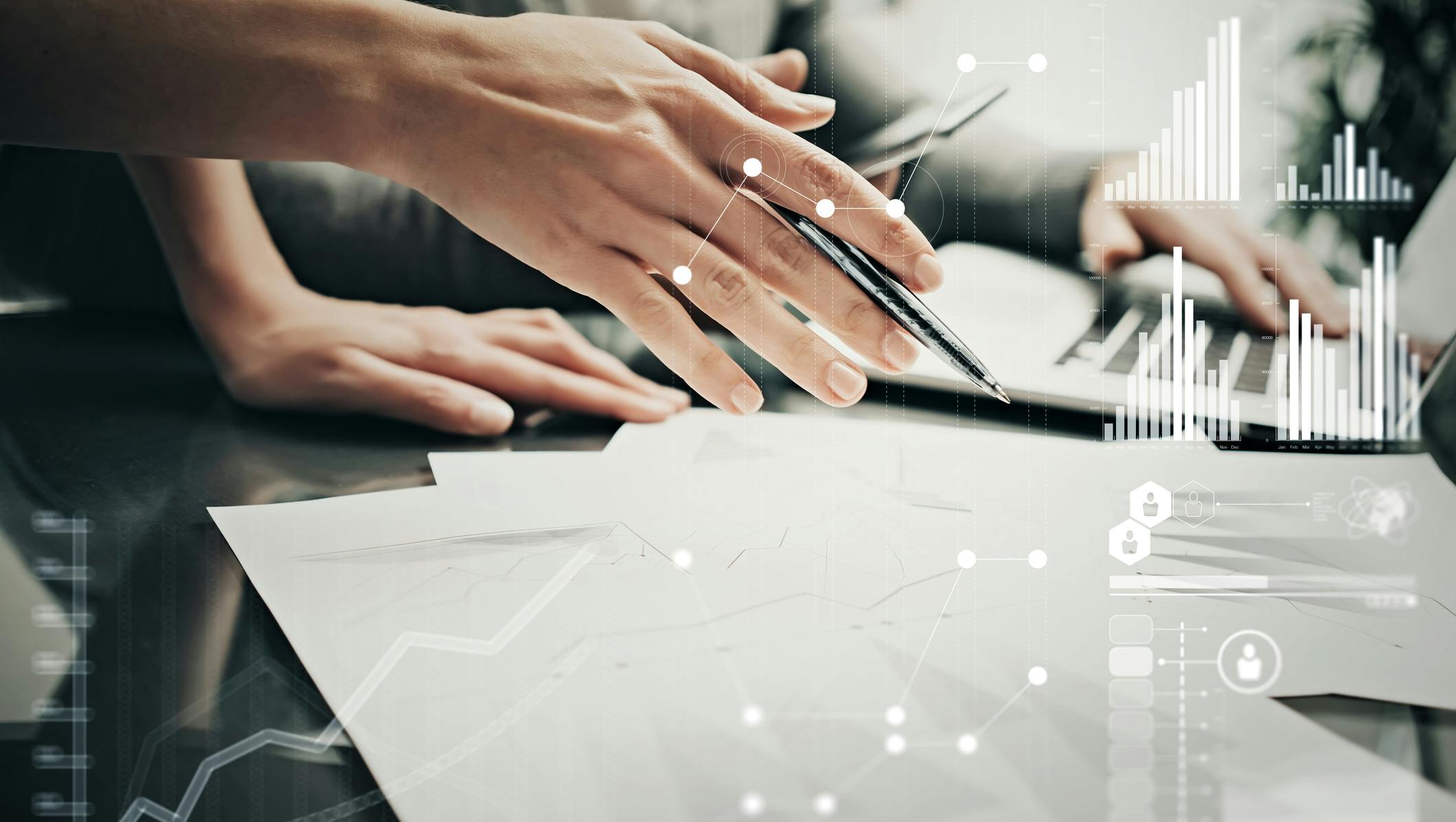 Hand holding pen hovering over paper. Stats and growth icons on screen