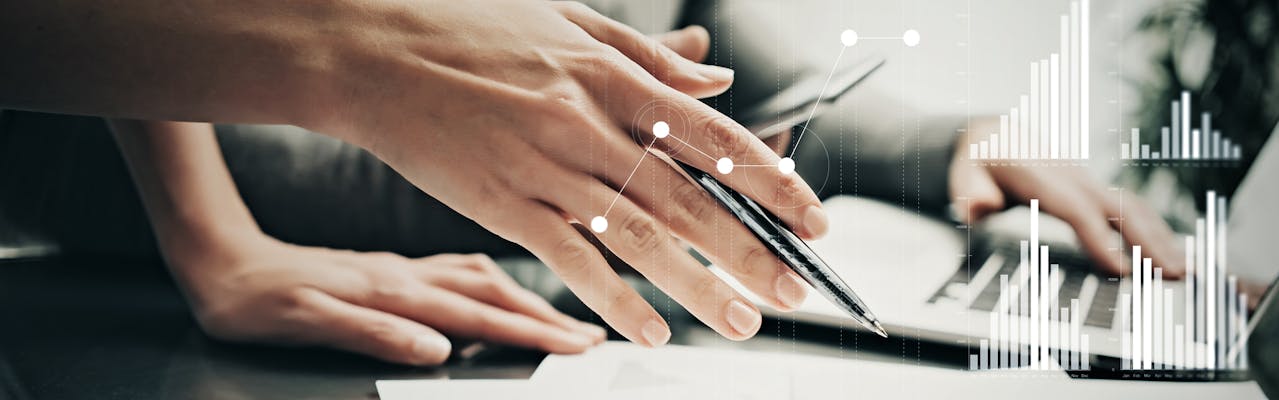 A hand holding a pen above sheets of paper. Stats and growth icons on screen.