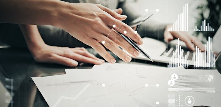 A hand holding a pen above sheets of paper. Stats and growth icons on screen.