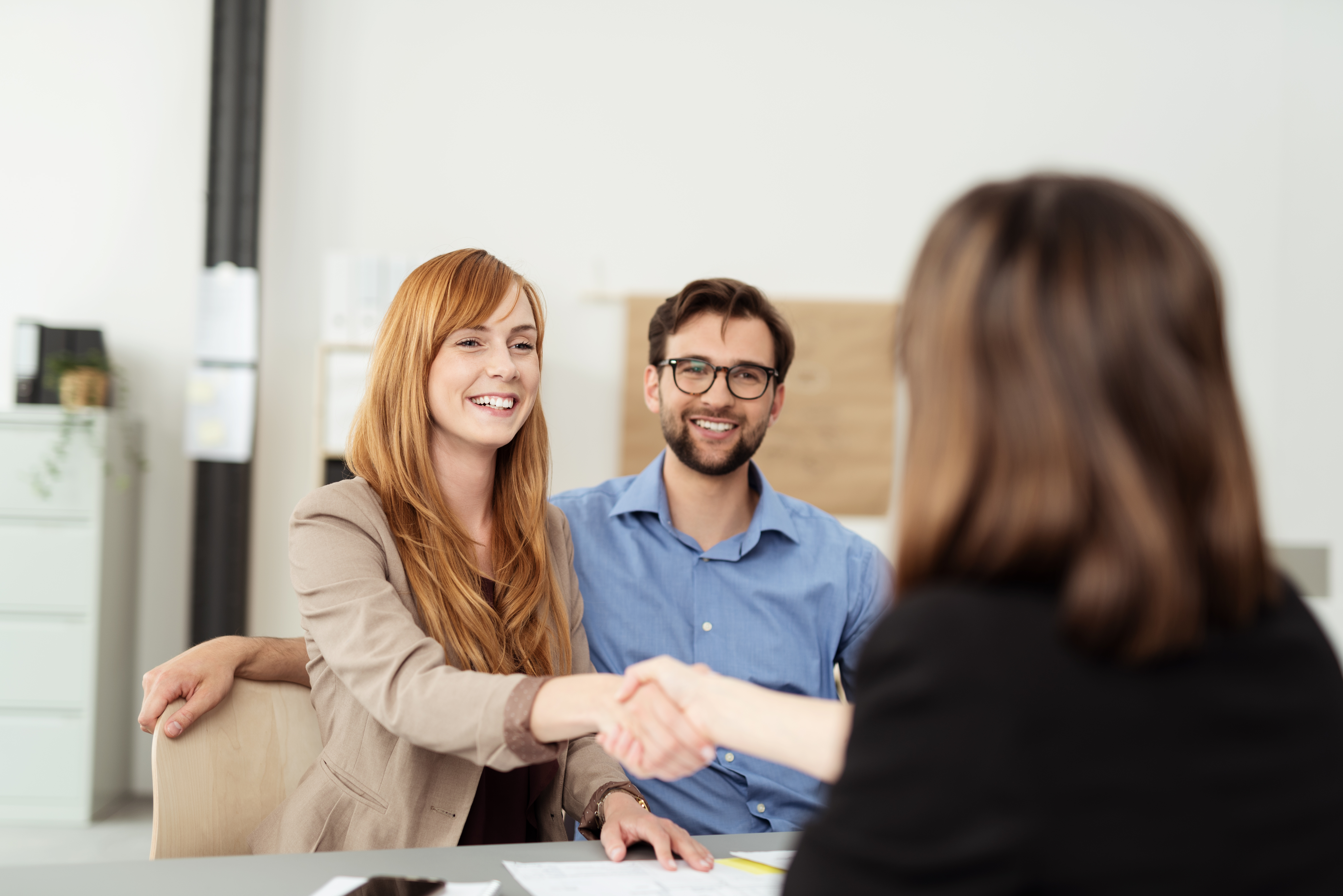 A friendly couple chatting with a banker. The woman is shaking the banker's hand.