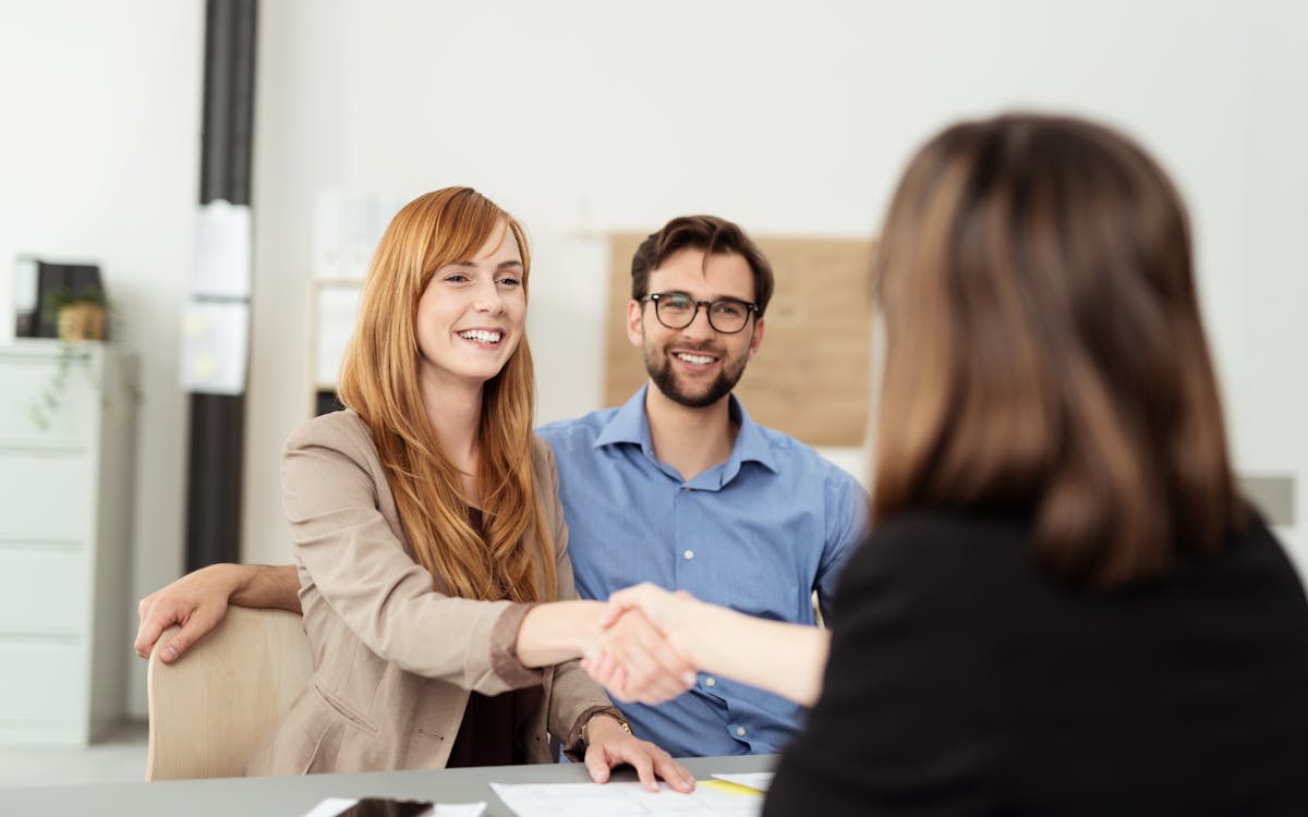 A friendly couple chatting with a banker. The woman is shaking the banker's hand.