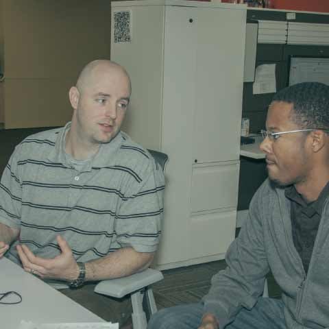 Two men seated at a desk, talking