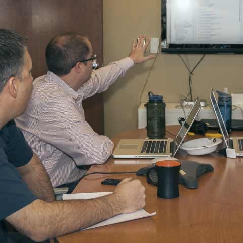 Two men seated in a conference room and looking at a large screen